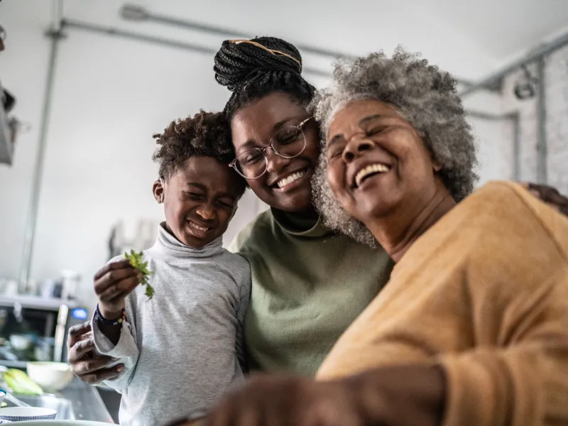 Grandmother, mother, and son smiling together while in the kitchen at home.