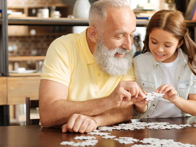 A grandfather puts together a puzzle with his granddaughter. 
