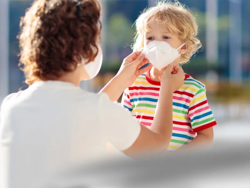 A mom helps her son position his face mask.