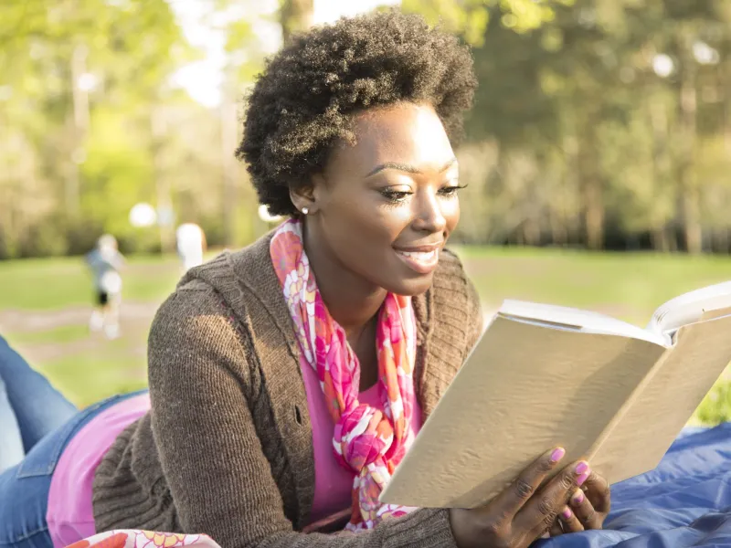 A woman reading a book outdoors.