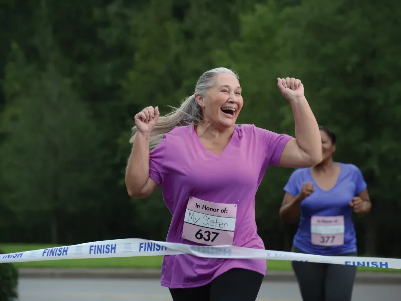 An older woman is ecstatic as she crosses the finish line of a charity foot race