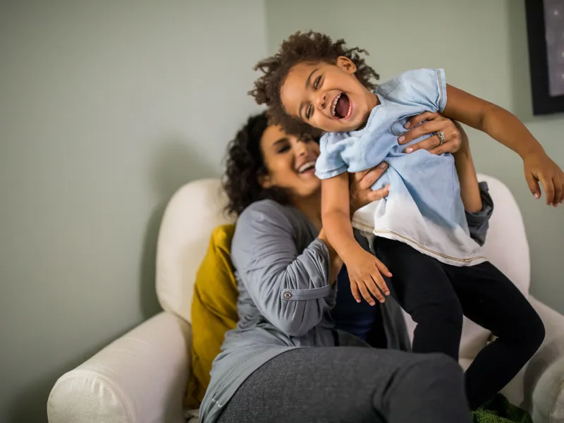 A pregnant woman playing with her child in the couch.