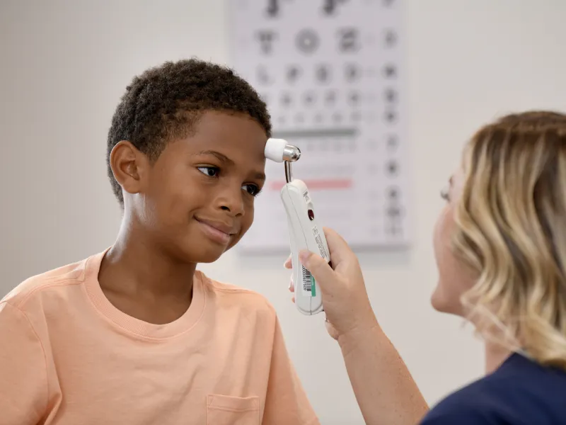 A Young Patient Smiles as a Primary Care+ Nurse Checks His Tempature