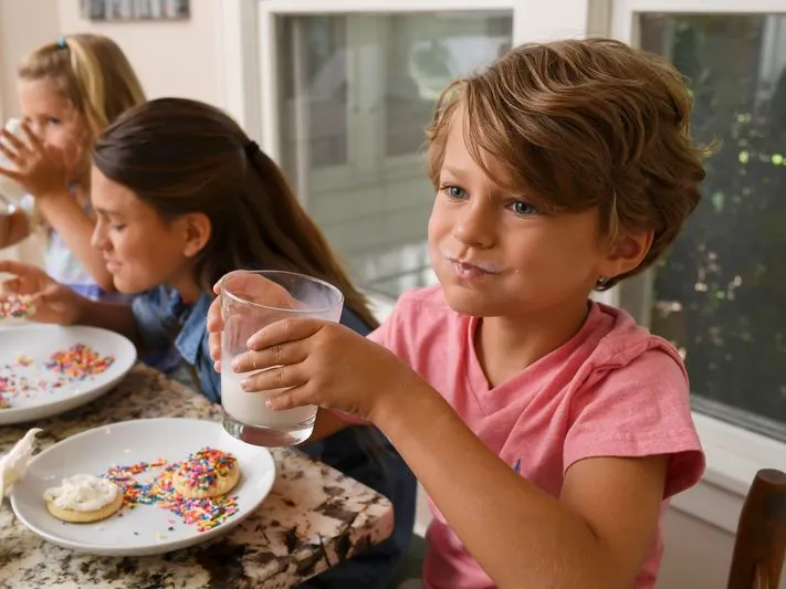 Three kids enjoy homemade cookies and milk