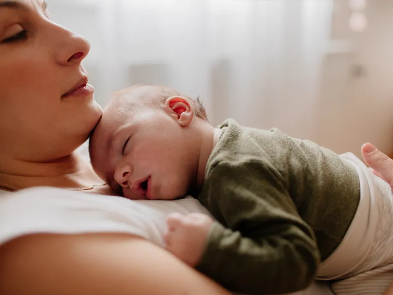 A serene mother cuddles with her sleeping newborn baby.