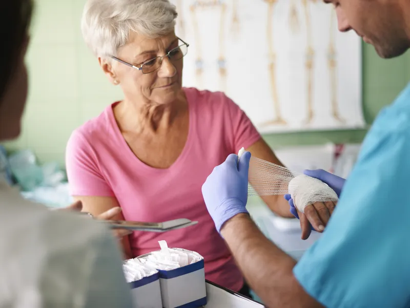 An older woman has her hand bandaged by a nurse