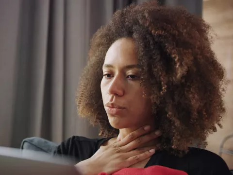 A woman touching her throat and showing discomfort