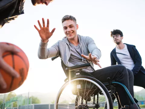 Older teens playing basketball one of which is in a wheelchair 