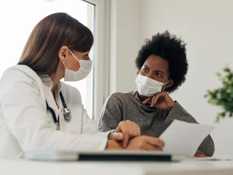 Doctor speaking to her patient about her treatment options while wearing masks in practice office