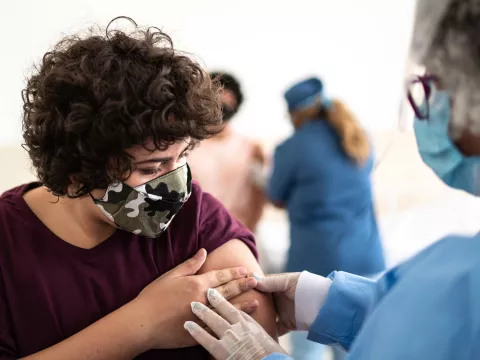 Woman wearing a mask get's a flu shot from a medical professional in blue scrubs
