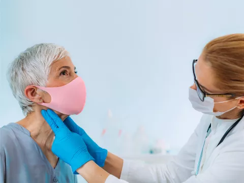 A Doctor examines a patient's neck while they both wear face coverings