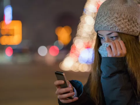 Woman outdoors bundled up in a beautiful winter's evening look at her cell phone