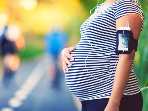 A pregnant woman rubs her belly while taking a break on a running trail.