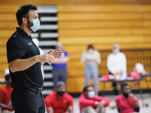 A masked man on stage giving a presentation