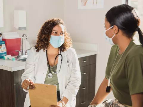 A Doctor Speaks to a Female Military Patient in an Exam Room.