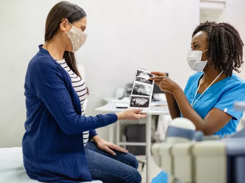 A Woman Looks Over The Sonogram of Her Baby with Her Physician.