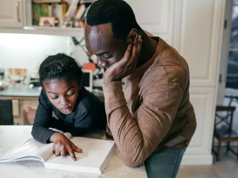 A Father Helps His Daughter Complete Her Homework in the Kitchen of Their Home.