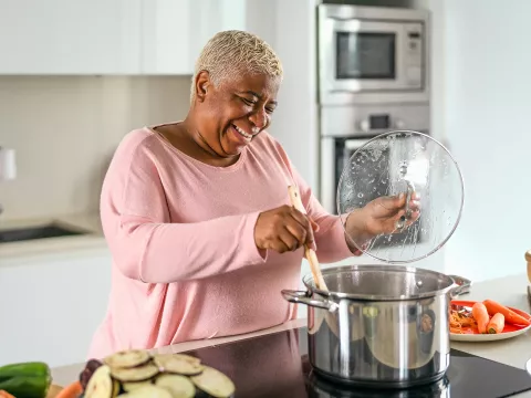 A Woman Gleefully Mixes a Large Pot on a Stove Top in a Modern Kitchen.