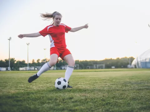 A Teenage Girl Soccer Player Kicks a Ball on the Pitch.