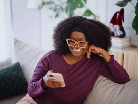 A Woman Smiles as She Reads Her Cell Phone on the Couch at Home.