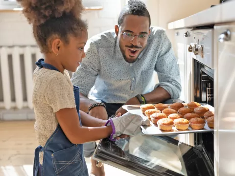 A Little Girl Pulls Muffins From an Oven While Her Father Watches