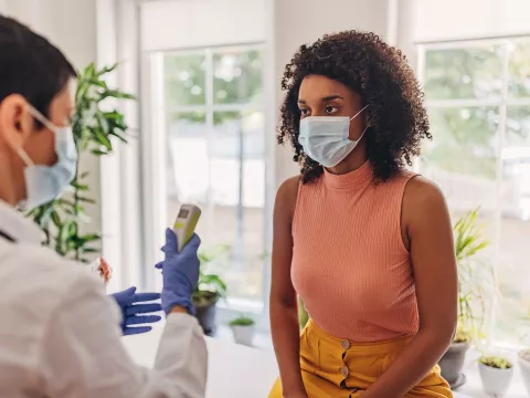 A Woman Wearing a Face Mask has her Temperature Taken by a Care Provider