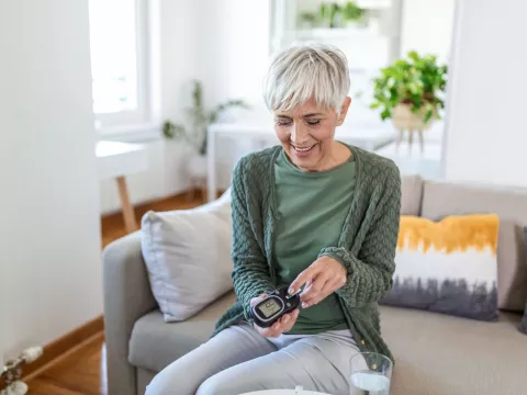 A mature woman taking an at-home diabetes test in her living room.