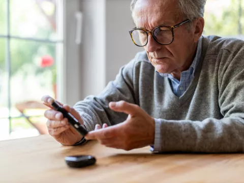 A Senior Checks His Glucose Levels with a Device While Sitting at the Kitchen Table