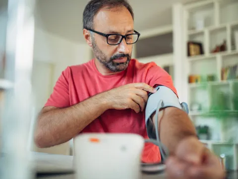 A Man Puts a Blood Pressure Cuff on His Arm in His Home.