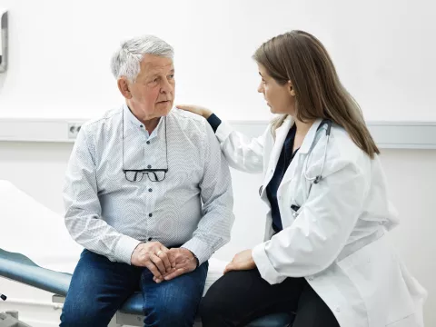 A Doctor Speaks Comfortingly With Her Senior Patient in an Exam Room 