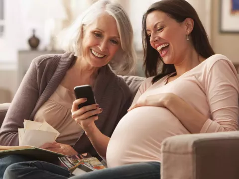A Mother Sits with Her Pregnant Daughter as they Laugh at Something on a Cell Phone