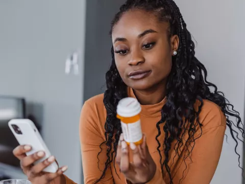 A Woman Examines a Pharmaceuticals Bottle While Holding Her Phone in the Other Hand