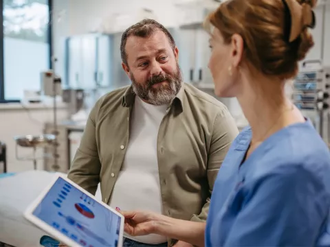 A Patient Speaks to a Provider in an Exam Room as She Goes Over His Vitals on a Tablet