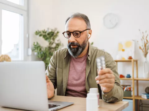 Man attending a virtual care appointment at home on laptop holding medication.