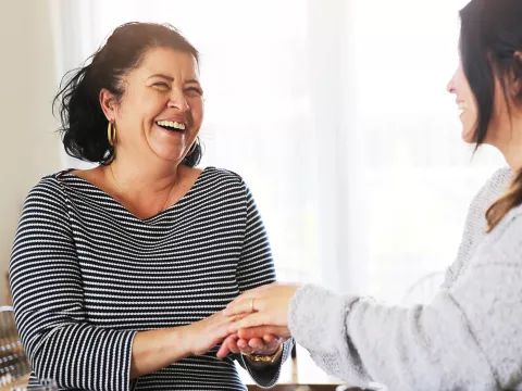 Two women, one holding another's hand, as she receives comfort from a friend after a cancer diagnosis.