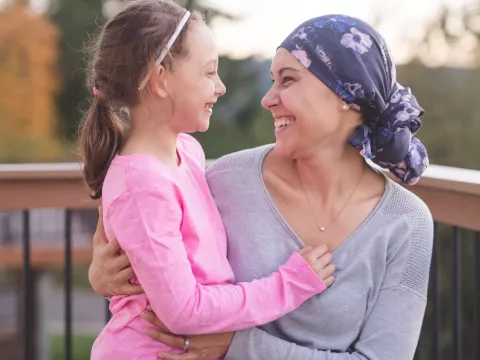 A mother and cancer survivor is sitting, with one arm around her daughter.