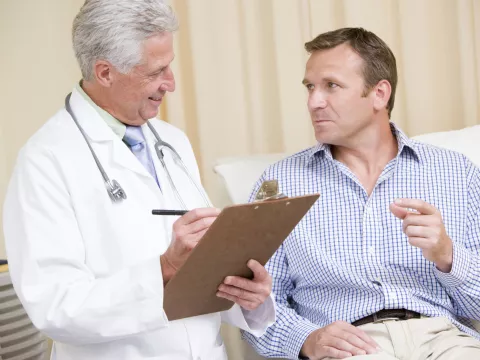 A doctor and his male patient (who is reclined) are consulting during an appointment.