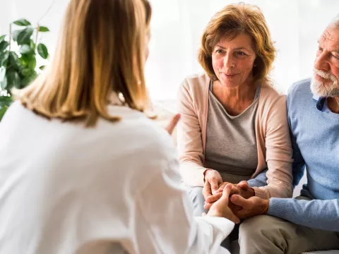 A senior couple, sitting down and holding hands, consulting a doctor at an appointment.