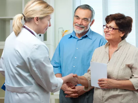 A couple meets their new doctor, the woman shakes hands with the doctor.