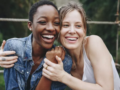 Two women, holding each other and grasping hands, smiling and laughing.