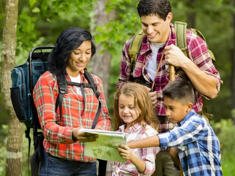 A family reads a map together while hiking in the woods.