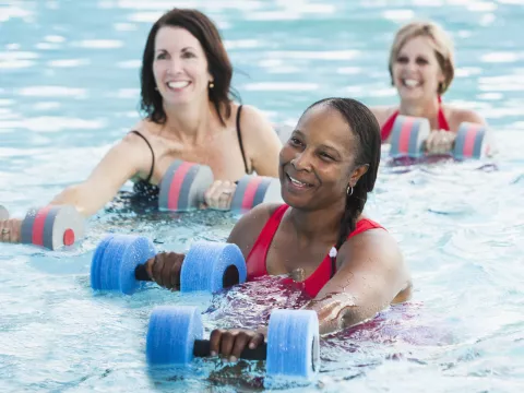 Three women building knee strength in a water aerobics class.