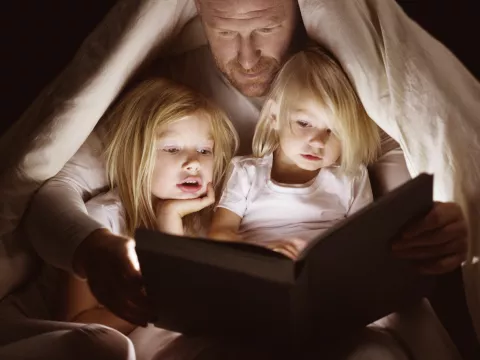 A dad reads to his daughters by flashlight.