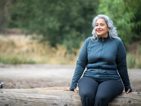 A Hispanic Woman Sits on a Log, Taking a Break From a Hike