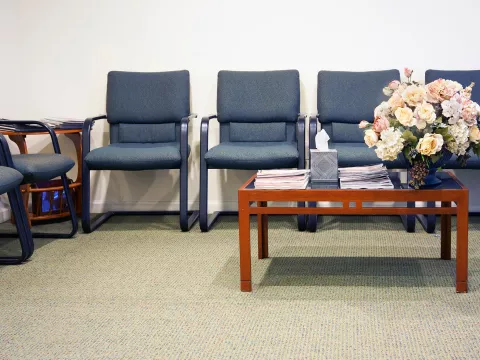 Hospital waiting room with blue chairs and a brown coffee table displaying flowers.