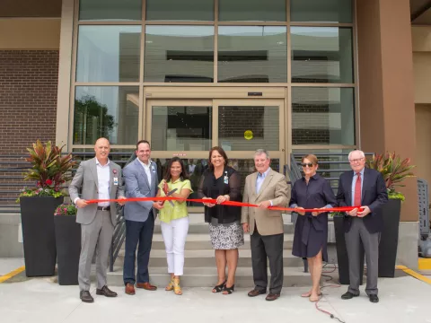 7 people prepare to cut red ribbon in front of new behavioral health building
