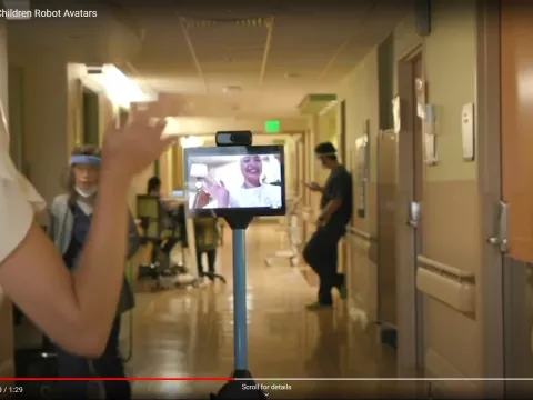 A child patient waves at a staff member in the hall as she controls her robot