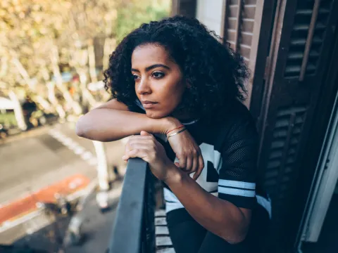 A Woman With a Concerned Look on Her Face Stares at Street From Her Balcony.