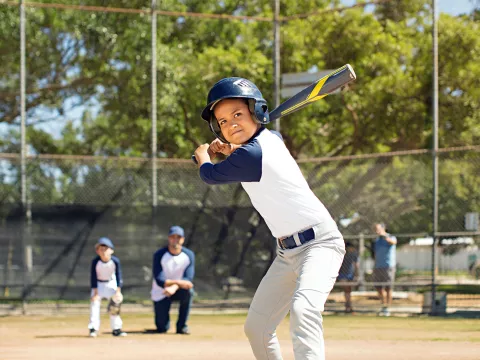 A boy playing baseball in the park with his father and his brother.