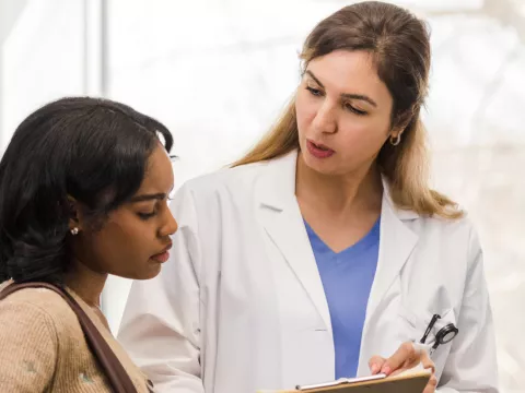 A young woman looks at a clipboard with her female doctor.